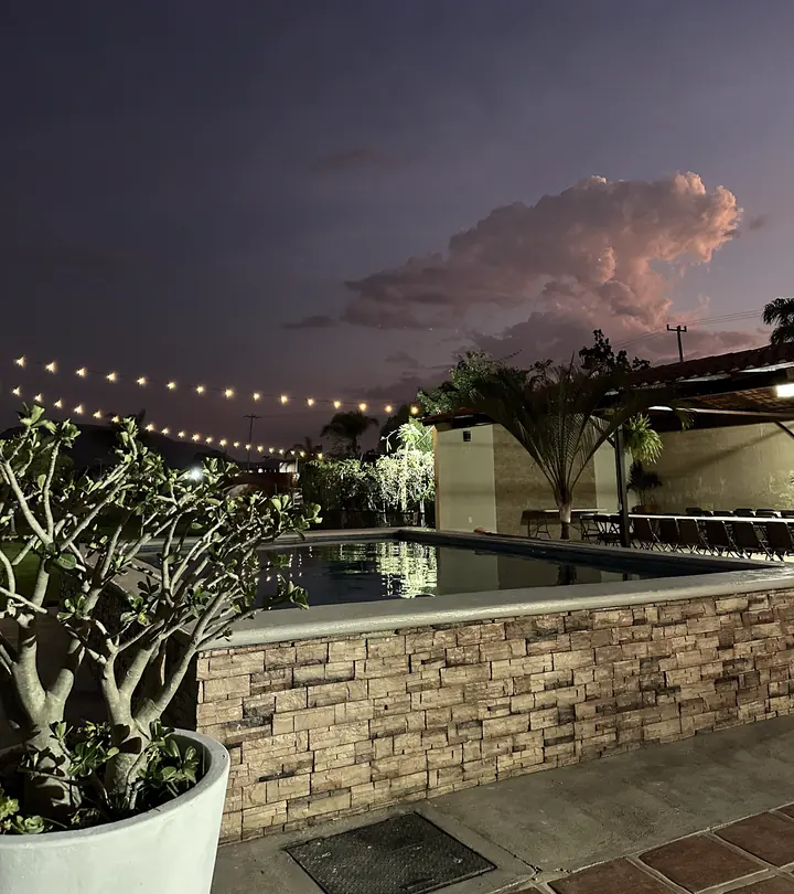 La terraza al atardecer: alberca iluminada, guirnaldas de luces, palmeras y mesas preparadas para un evento.
